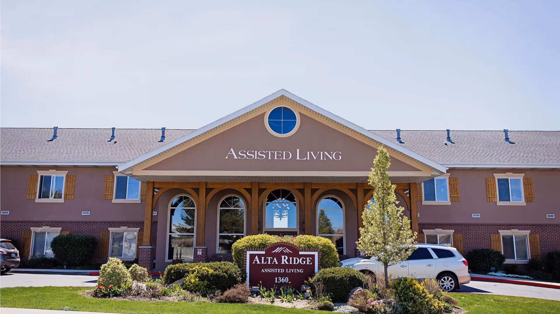 Front exterior of Alta Ridge Assisted Living building with a covered entrance, landscaping, and a sign that reads 'Alta Ridge'.