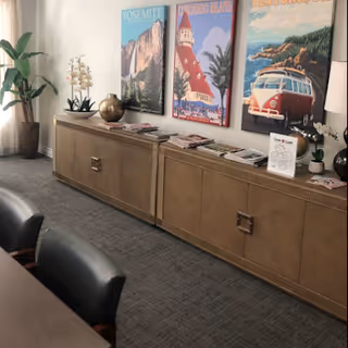 Interior common room with a long wooden sideboard topped with decorative plants and magazines and three colorful travel posters on the wall, with chairs visible in the foreground.