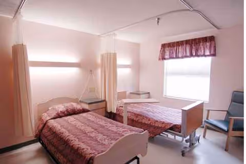 Two hospital-style beds separated by curtains in a bright patient bedroom