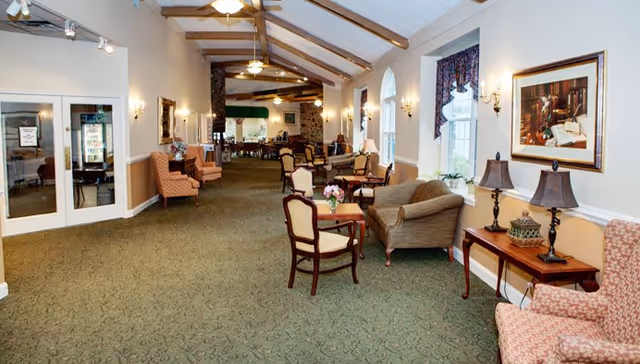 Spacious common lounge with upholstered chairs, sofas, small tables, and a vaulted ceiling with exposed beams.