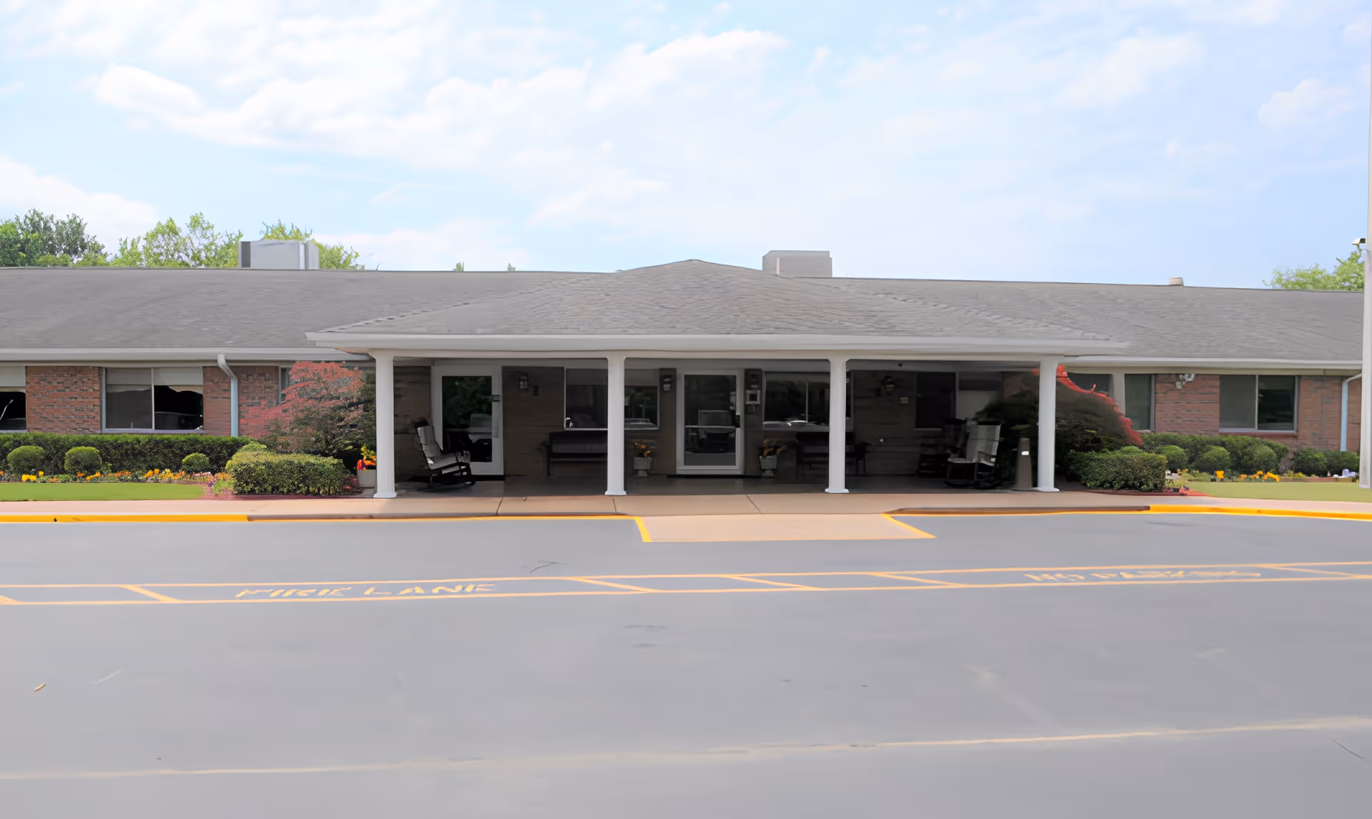 Front entrance of a single-story brick nursing facility with a covered portico, white columns, landscaping, and a paved driveway.