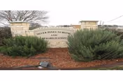 Stone sign for Silver Pines Nursing and Rehabilitation Center surrounded by green bushes and mulch with a tree and building visible in the background under a cloudy sky.