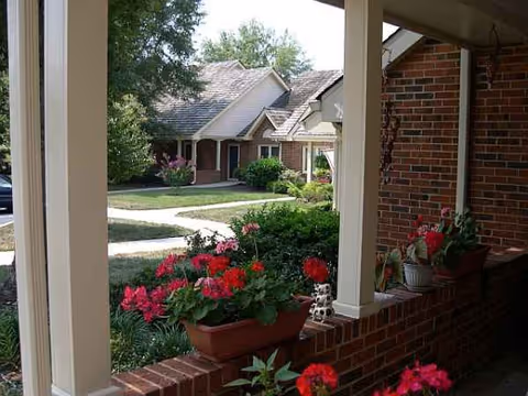 Brick porch with planters and blooming red flowers along a residential senior living complex.