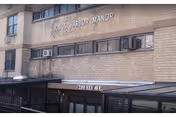 Exterior view of a brick building with the sign 'Kings Harbor Manor' mounted on the wall above a covered entrance. The address '2355 Ely Ave' is displayed above the entrance door.