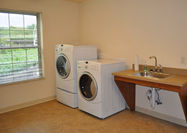 A bright laundry room with two front-loading washer/dryer units beside a utility sink and a window.