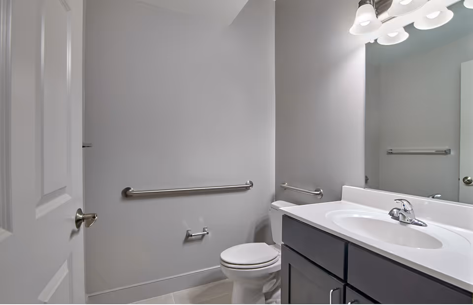 Accessible bathroom with a toilet, sink and vanity beneath a mirror and wall-mounted grab bars.