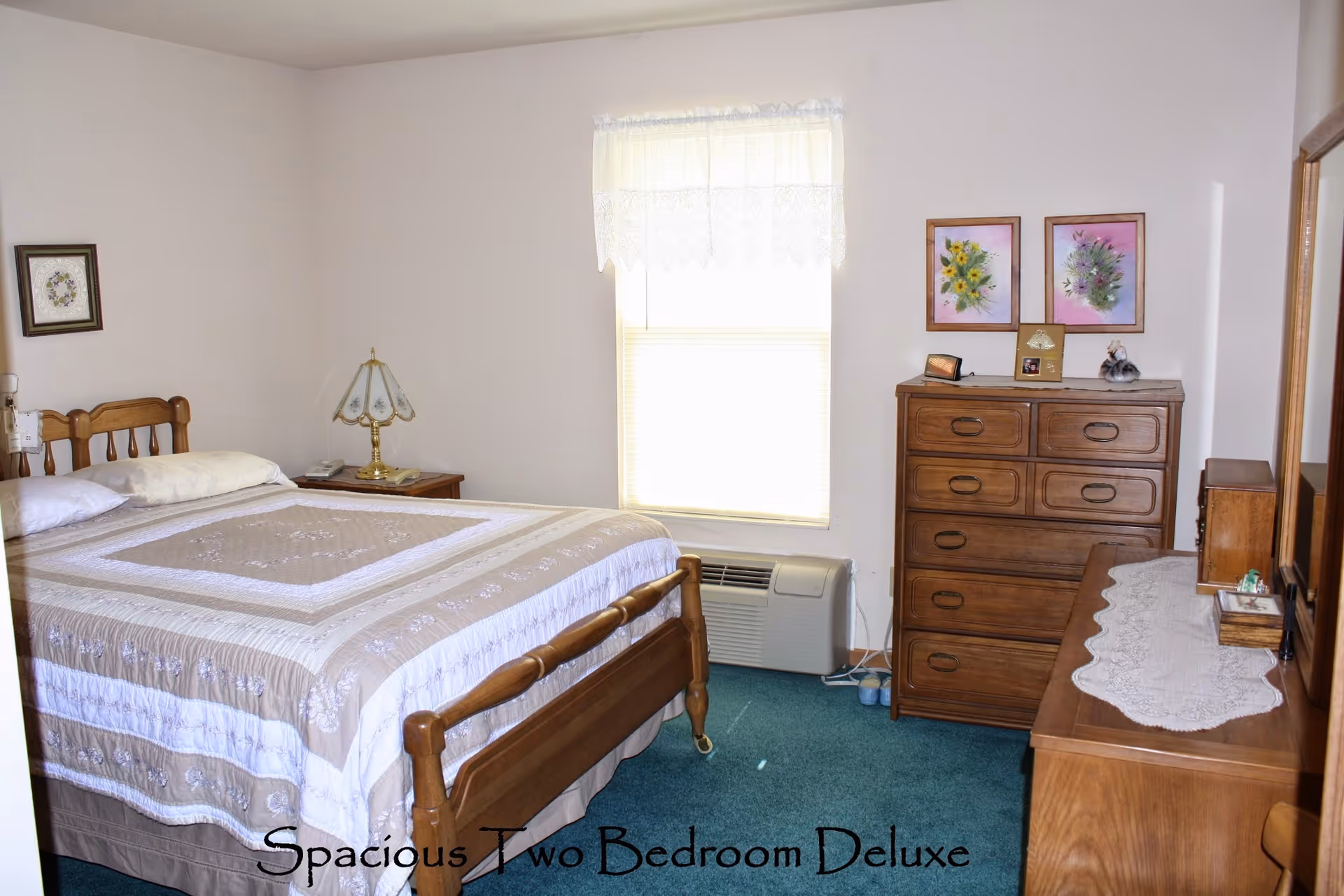 Bright bedroom with a wooden bed, matching dressers, a window with lace curtain and an air conditioning unit.
