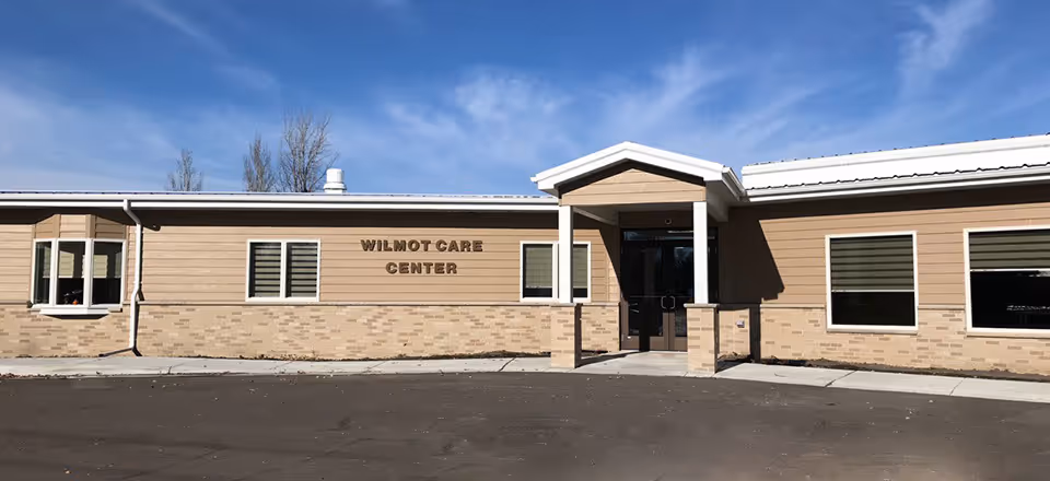 Single-story care center building exterior with a central entrance and a sign reading 'Wilmot Care Center'.