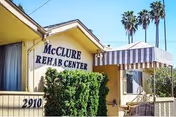 Front exterior of McClure Rehab Center with striped awning and palm trees.
