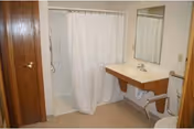 Accessible bathroom featuring a walk-in shower with curtain, a wall-mounted sink and mirror, and a toilet with grab bars.