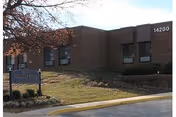 Brick single-story healthcare facility building with a small lawn, an entrance sign, and the address number '14200' visible on the facade.