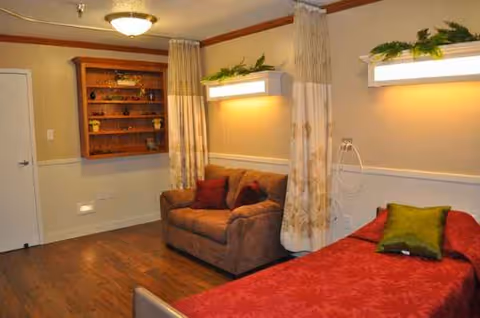 A cozy senior living interior with a bed, sofa, curtains, shelves, and warm lighting.