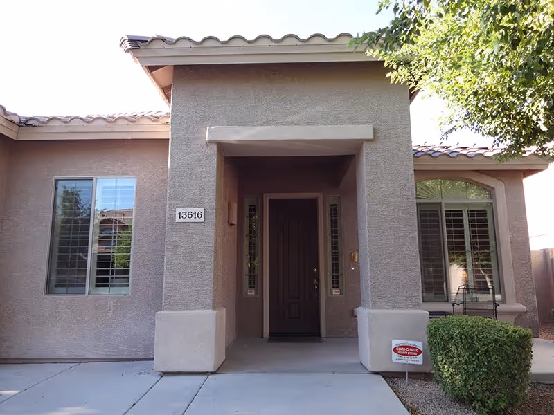 Front entrance of a stucco house with a recessed doorway, flanking windows, tiled roof, and address number 13616.