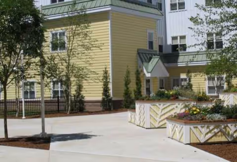 Exterior view of a yellow Merrimack County Nursing Home with planters and trees.