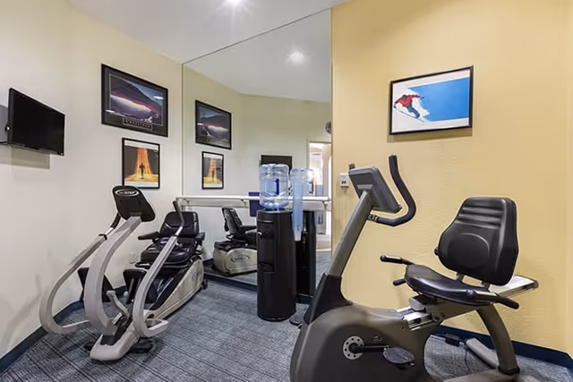 Small fitness room with two cardio machines, a recumbent exercise bike, a water cooler, mirrored wall and framed posters.
