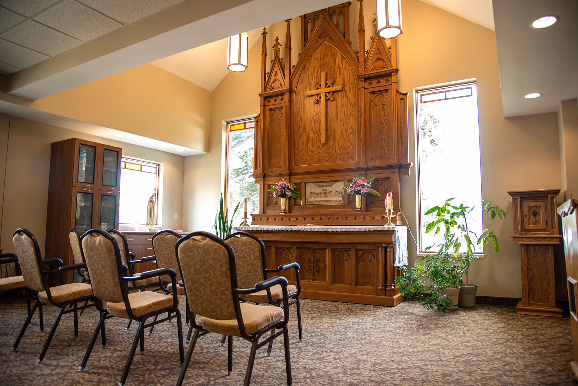 Small chapel-style interior with rows of upholstered chairs facing a wooden altar and tall windows.