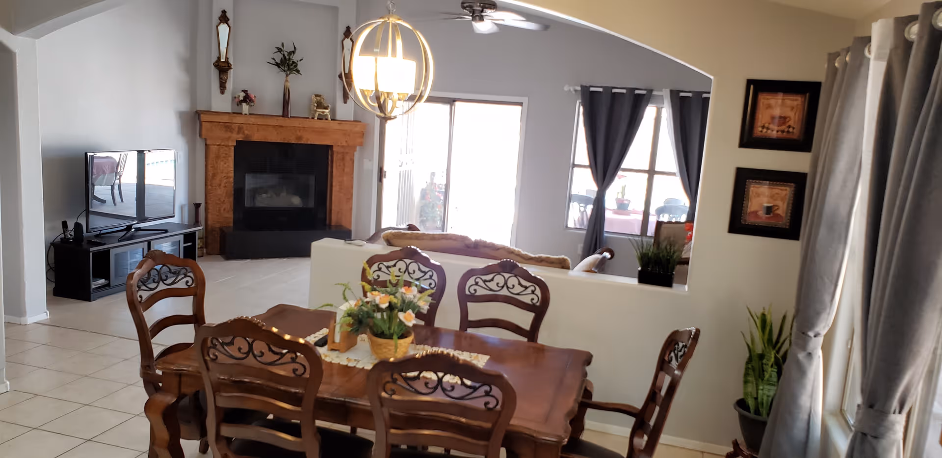 Sunlit open-plan dining area with a wooden table and chairs overlooking a living room with a fireplace and TV.