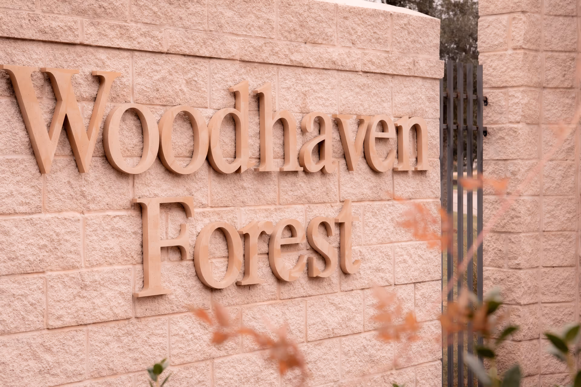 Entrance stone wall sign that reads 'Woodhaven Forest' with plants blurred in the foreground.