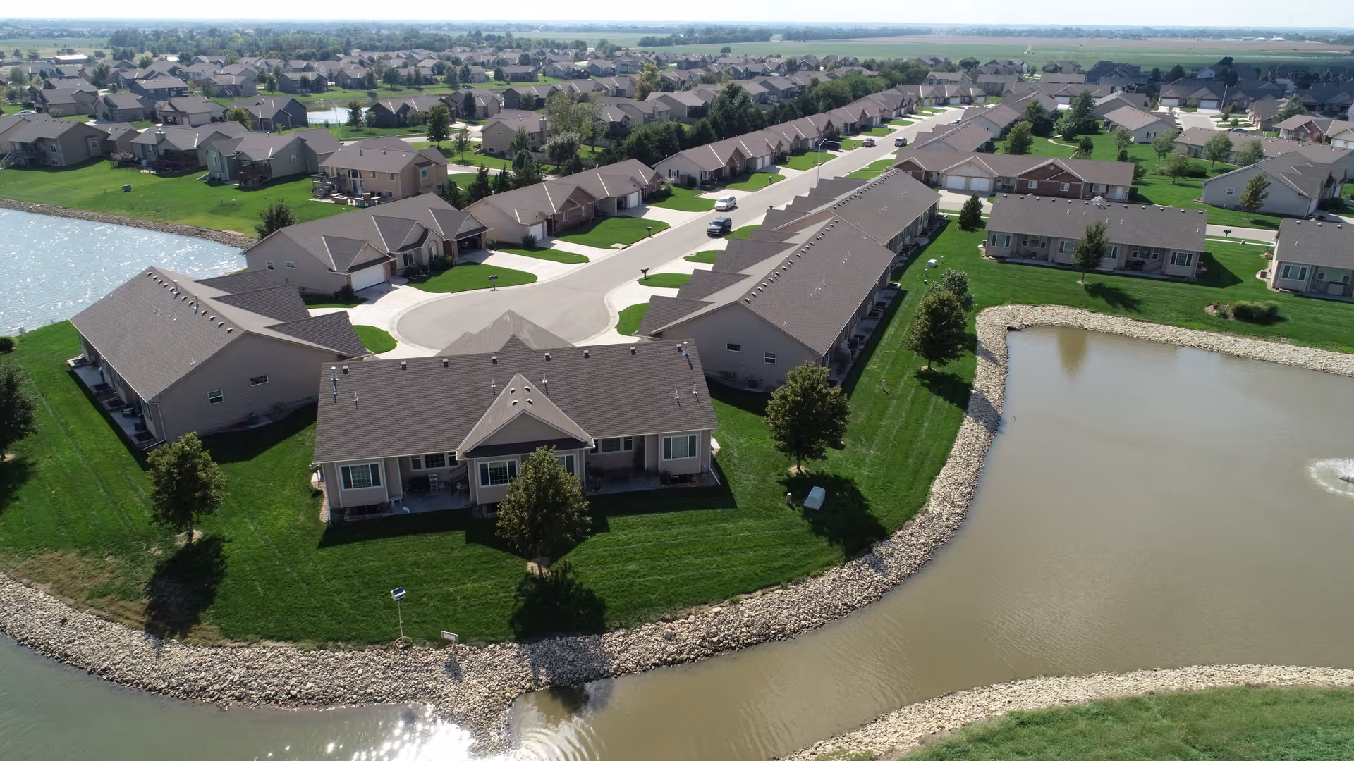 Aerial view of single-story villa units arranged around a pond in a suburban senior living community.