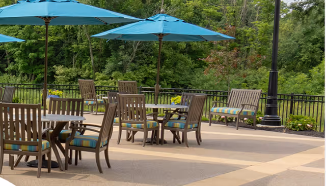Outdoor patio with tables, chairs, and teal umbrellas overlooking a wooded area.