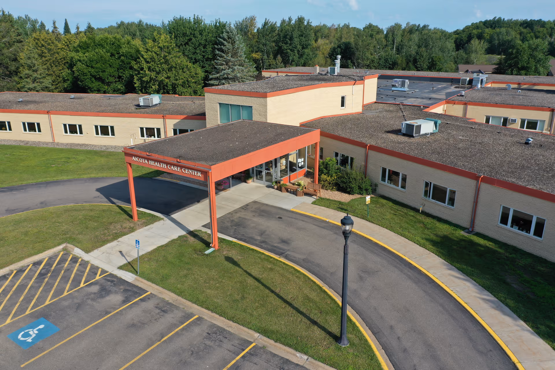 Aerial view of Aicota Health Care Center's front entrance with a covered drop-off, driveway, and adjacent parking.