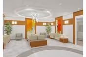 A spacious and modern nursing center common area with light-colored tiled floors and white walls accented by wooden panels and colorful abstract artwork. The room features multiple cushioned chairs and sofas arranged around small wooden tables. Two tall green plants are placed near the walls, and a contemporary chandelier hangs from a circular recessed ceiling light.
