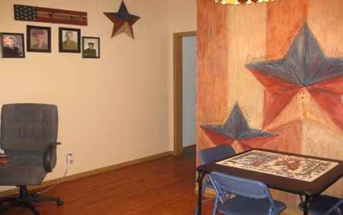 Indoor senior living activity room featuring a large star mural, framed photos, and a puzzle table.