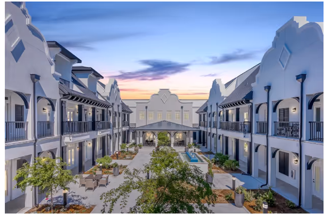 Two-story white residential building surrounding a landscaped courtyard with seating and a small pool at sunset.