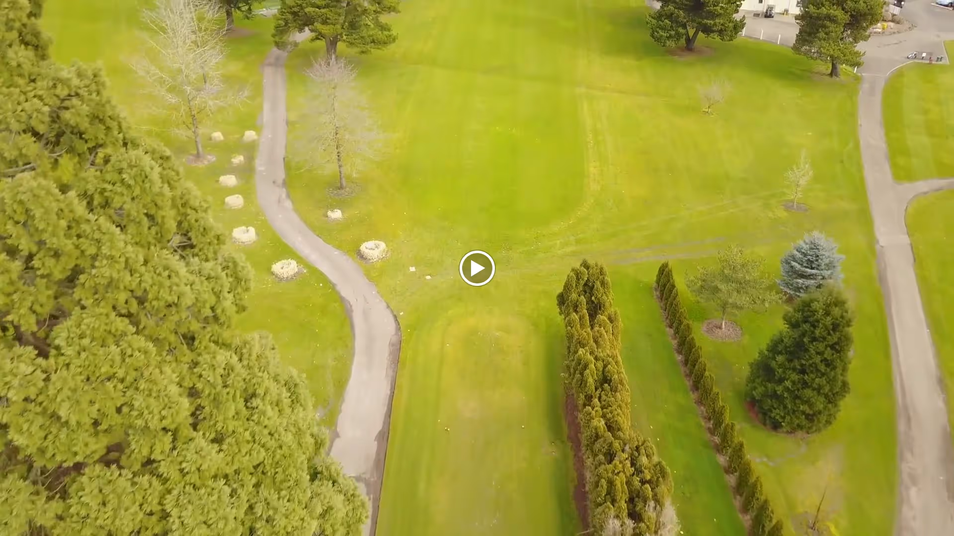Aerial view of a green golf course with neatly trimmed grass, trees, and paved walking paths winding through the landscape.