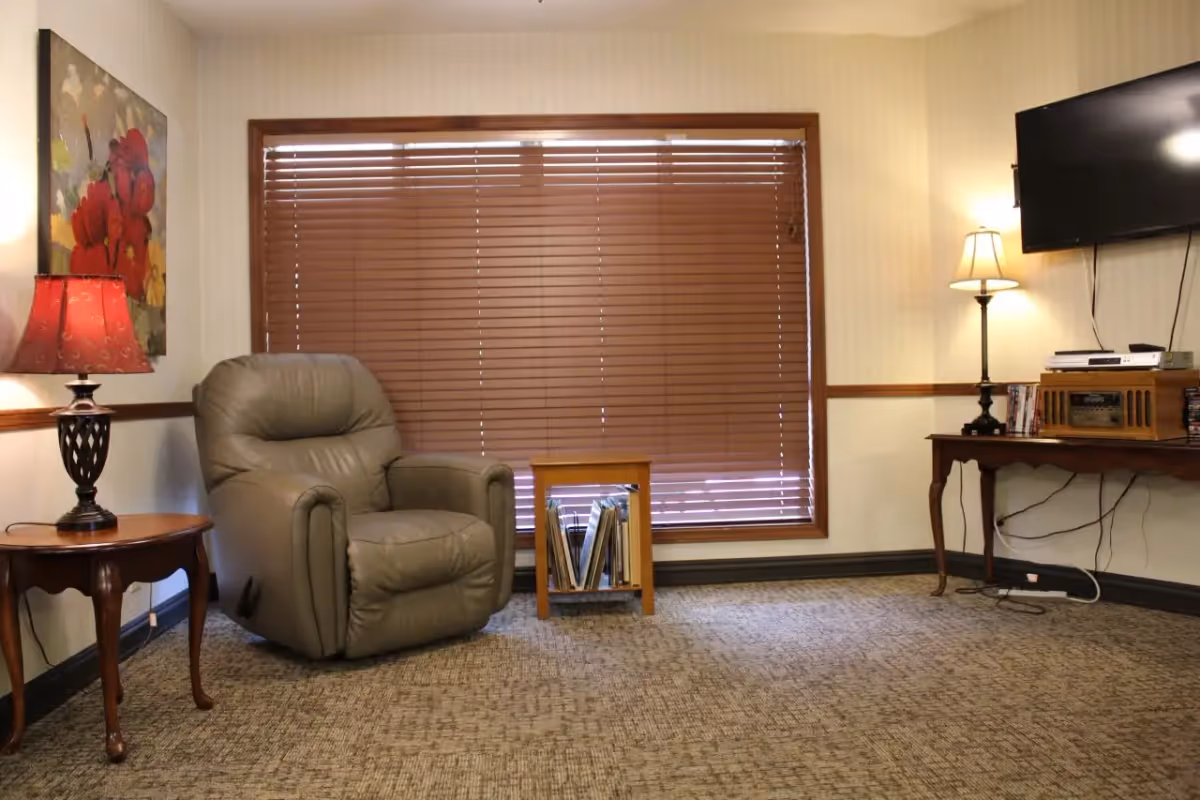 Cozy sitting area with a leather recliner, side tables and lamps in front of a window with closed blinds.