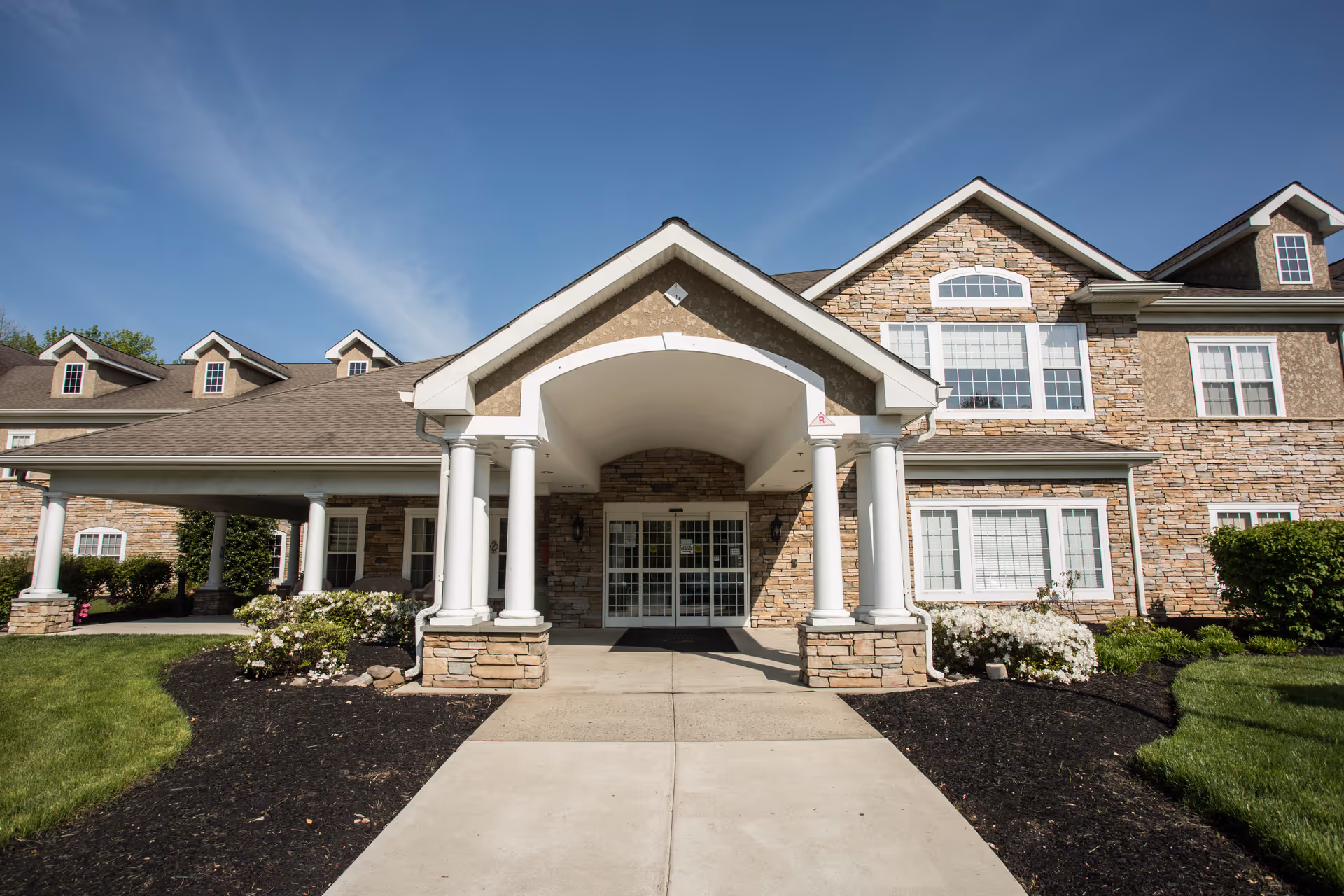 Front entrance of a stone-faced residential building with a covered porte-cochere supported by white columns.