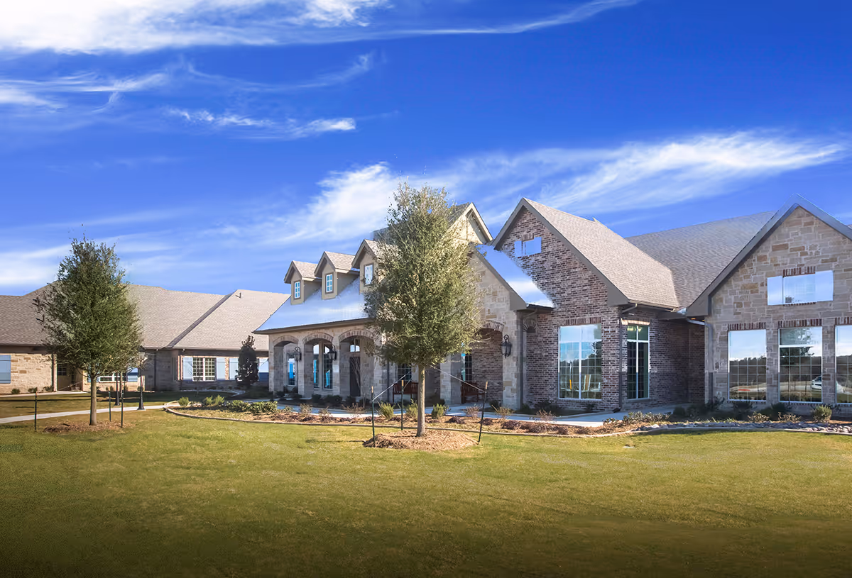 A single-story stone and brick senior living facility sits on a green lawn under blue sky.