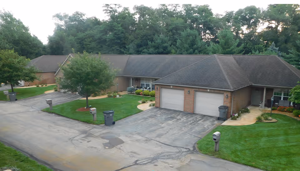 Single-story brick residences with attached garages, driveways, mailboxes, and neatly landscaped lawns in a tree-lined setting.