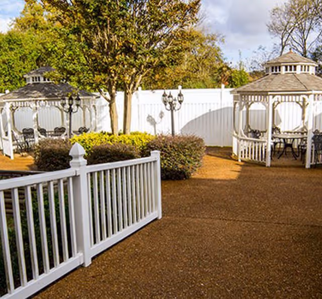 Outdoor courtyard with white gazebos, a white fence, paved walkway, and landscaping.