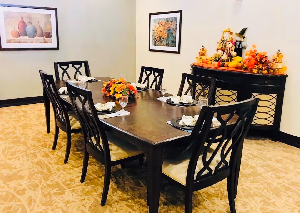 Formal dining room with a dark wooden table set for six, a fall floral centerpiece, and a decorated sideboard.