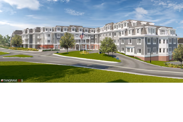 Exterior front view of a multi-story senior living facility with a circular driveway, landscaping, and an American flag under a blue sky.