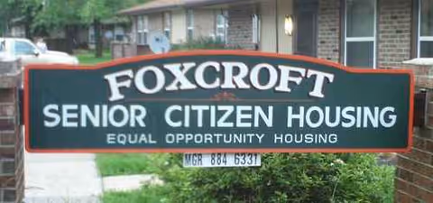 Exterior sign reading FOXCROFT SENIOR CITIZEN HOUSING in front of a brick building