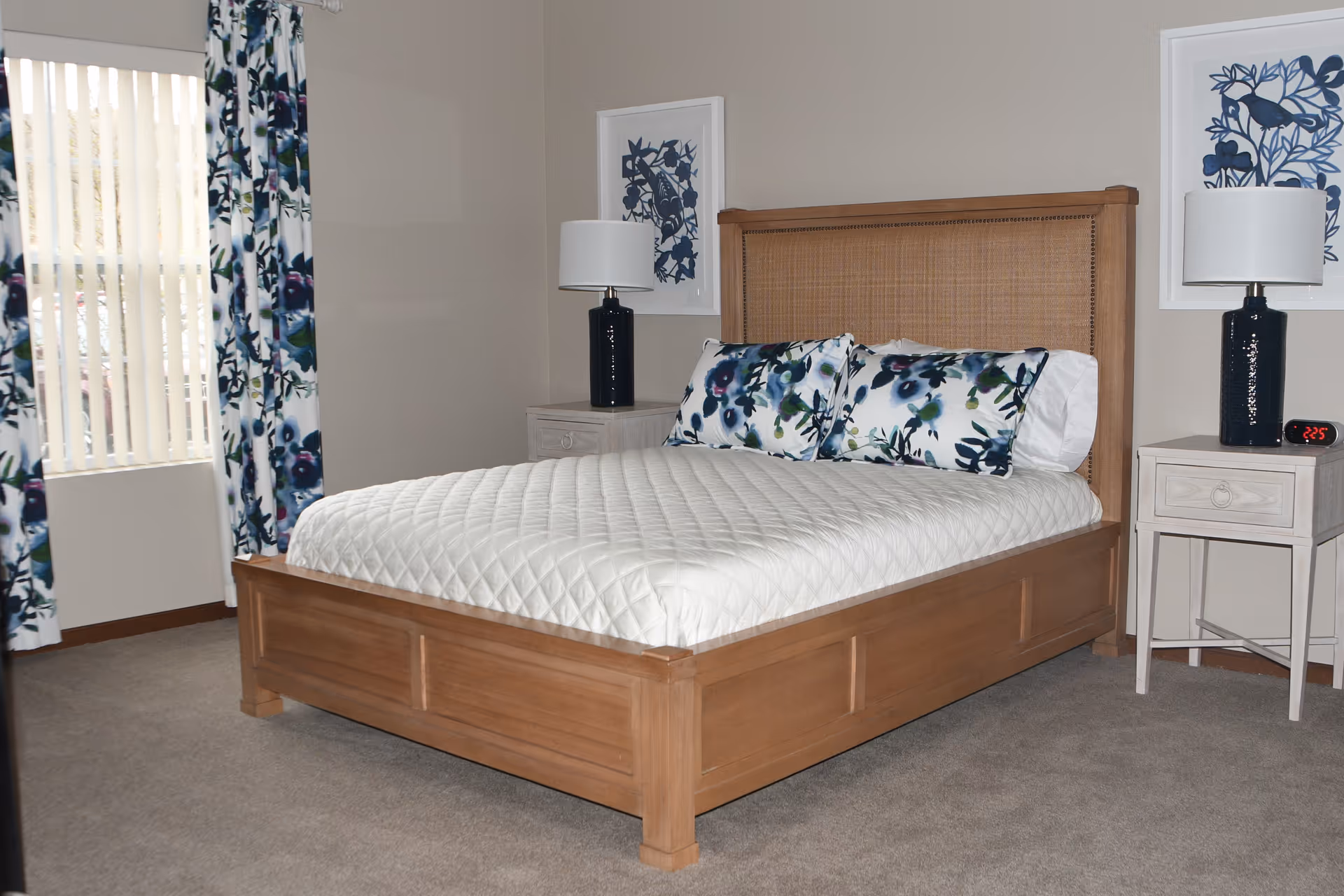 A neatly made bed with a wooden frame, floral pillows, nightstands and lamps in a furnished bedroom.