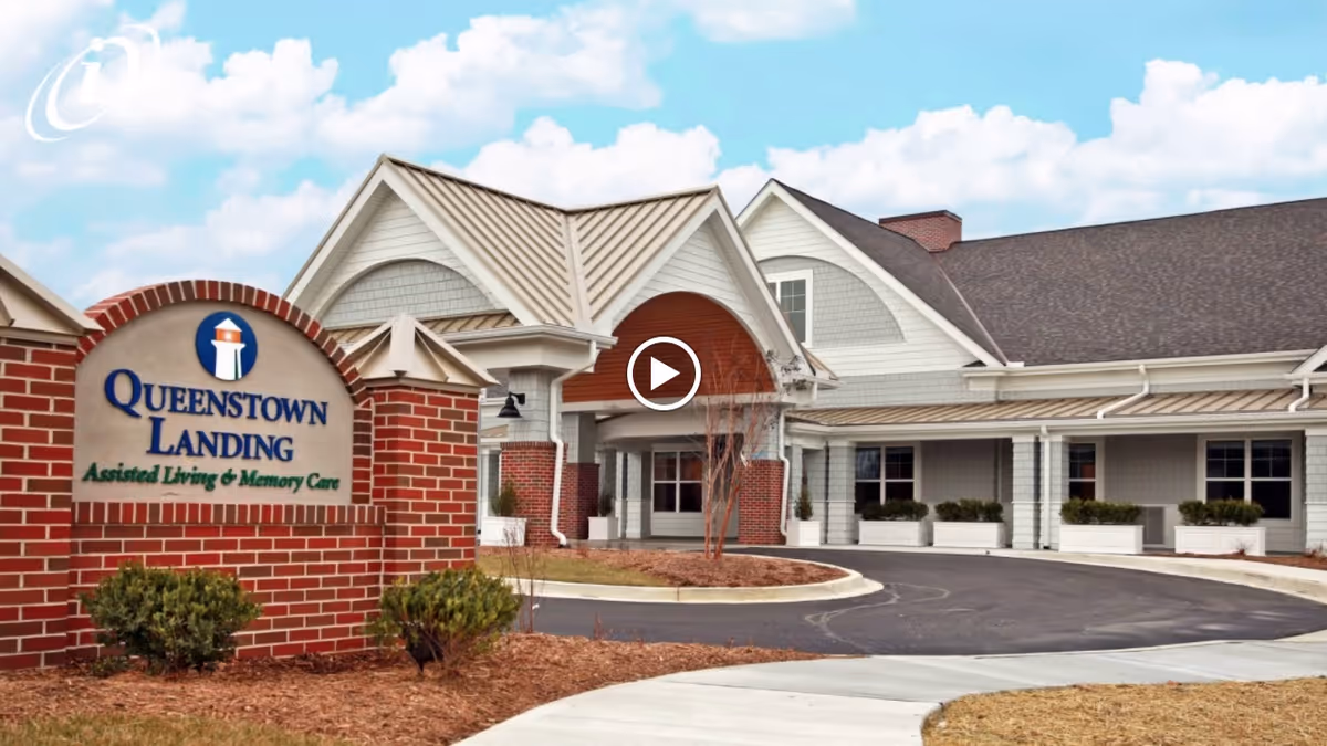 Front entrance of Queenstown Landing assisted living and memory care facility with a brick sign and circular driveway.