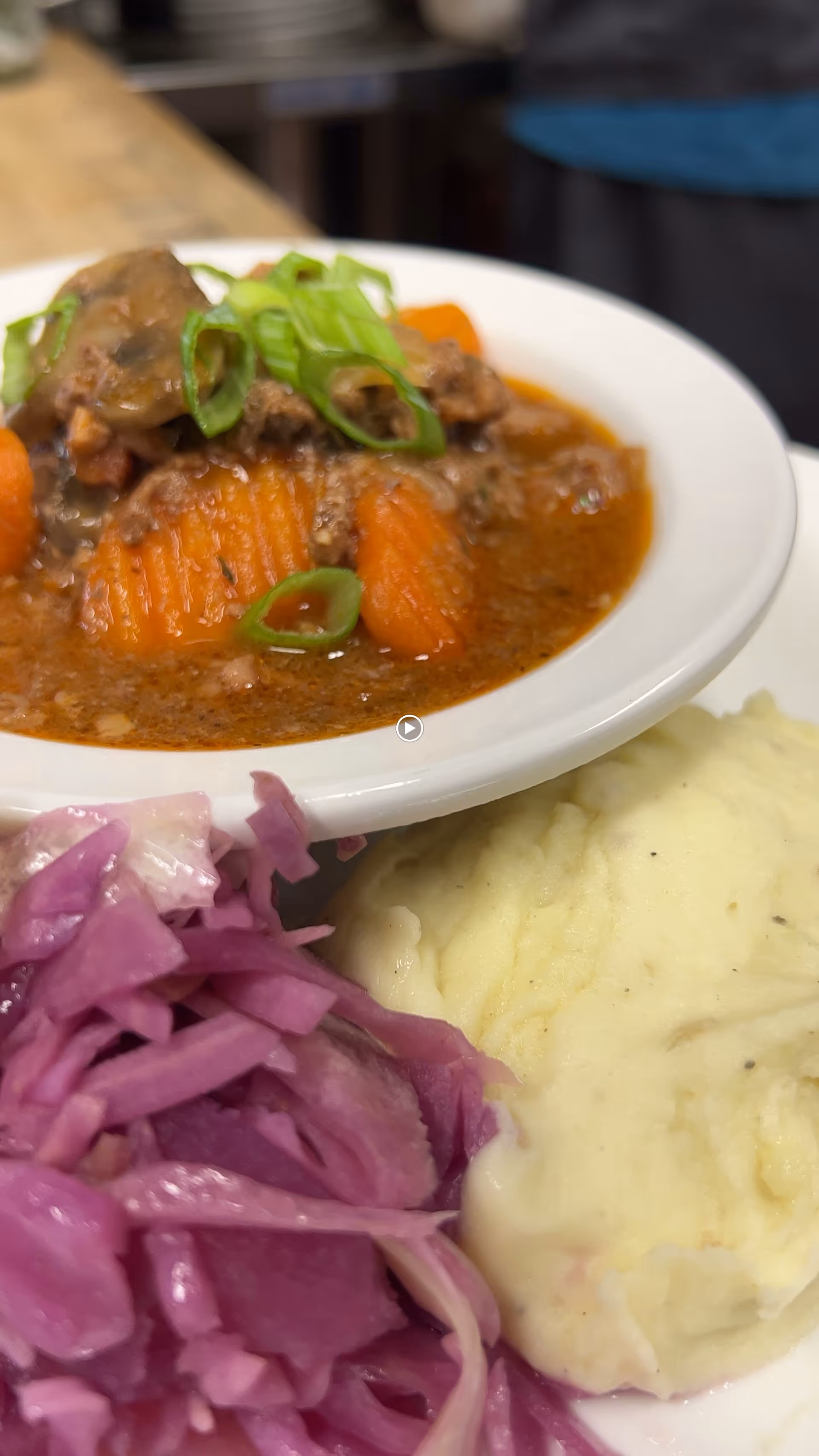 Close-up of a plate with beef stew and carrots, mashed potatoes, and pickled red cabbage.