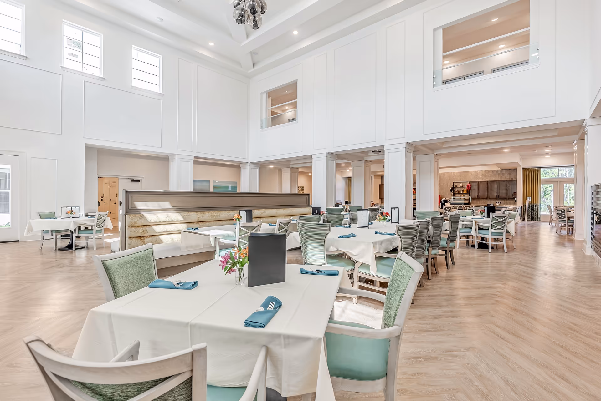 Bright, spacious dining room with multiple set tables, pastel chairs, and high ceilings.