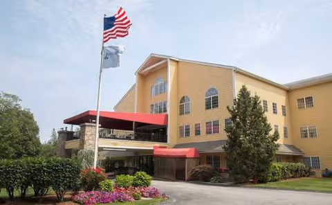 Front exterior of Greenwich Farms at Warwick, a yellow building with red awnings and flags.