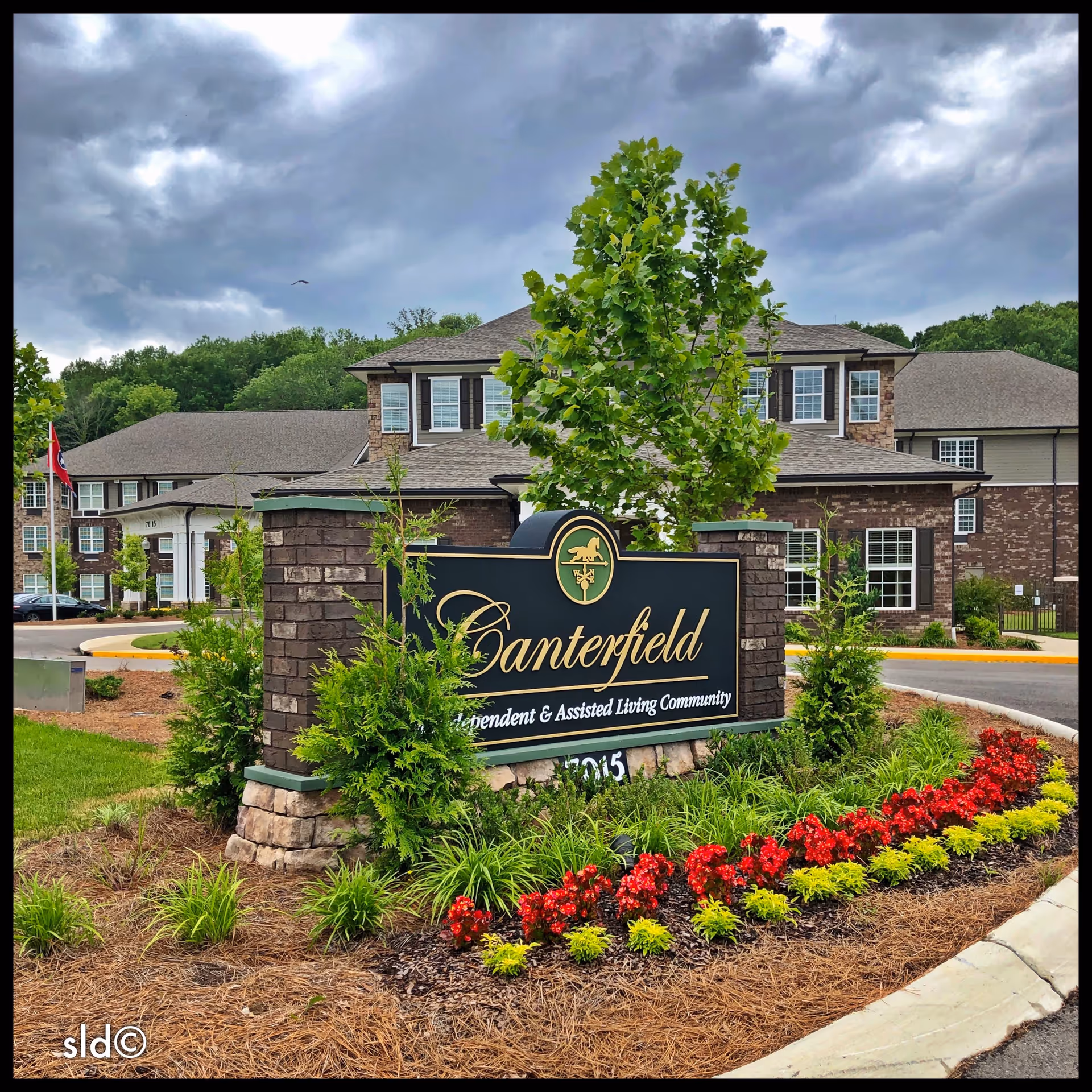 Stone and brick entrance sign reading 'Canterfield' at a landscaped driveway with the senior living building behind it.