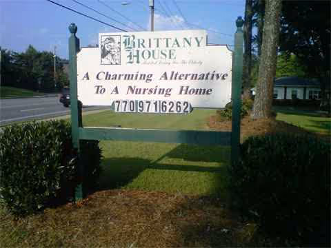 Outdoor sign for Brittany House senior living beside trees and a grassy landscape.
