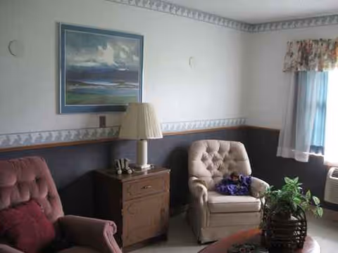 Cozy living room with pink armchair, beige chair, lamp, seascape painting, and a window.