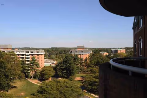 View from a balcony overlooking trees and multiple brick senior living buildings under a clear sky.