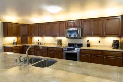 Long commercial-style kitchen with dark wood cabinets, marble countertops, and stainless steel appliances.
