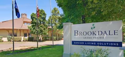 Exterior view of Brookdale Grand Prairie with a large sign and building in background.
