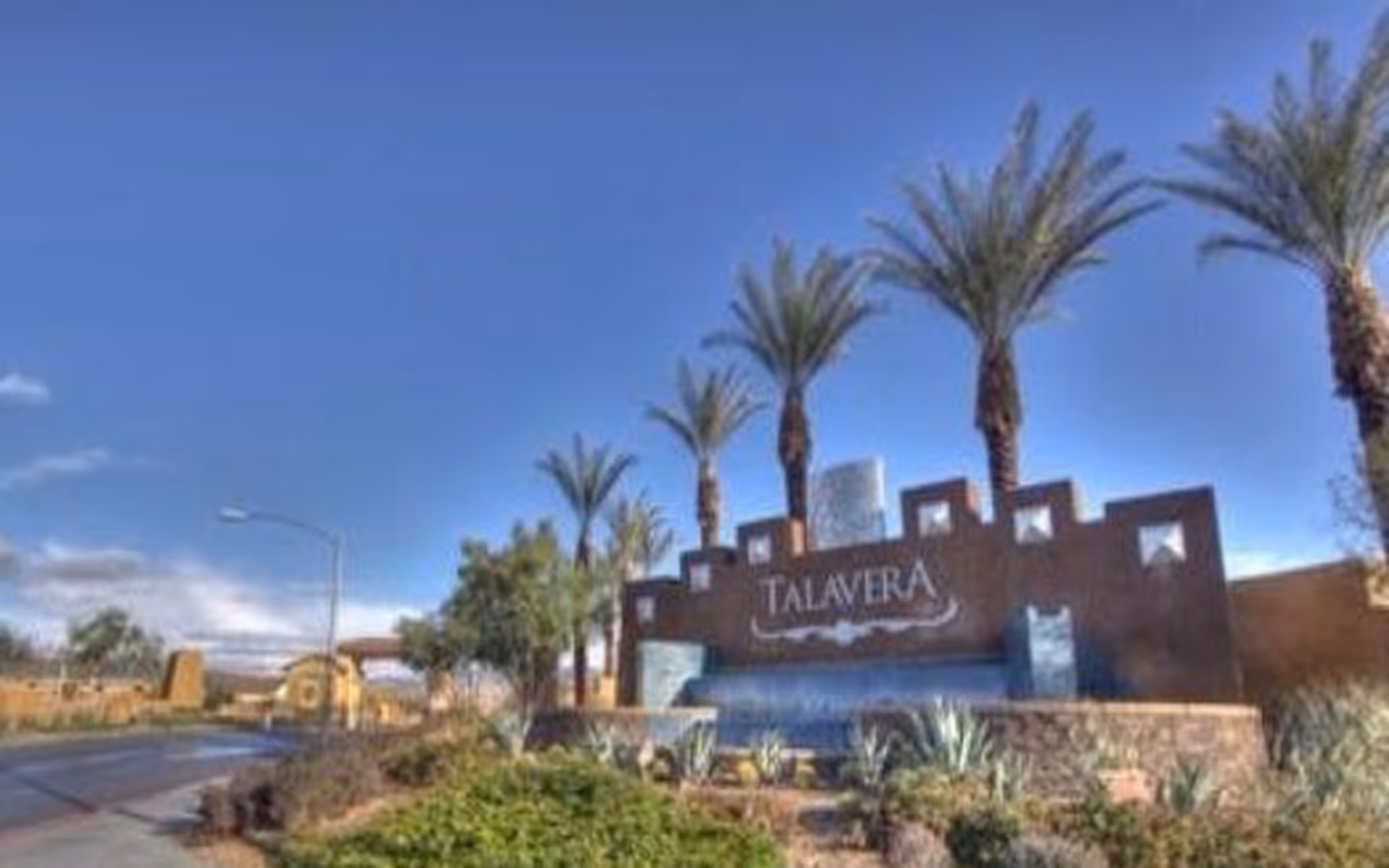Entrance sign for Talavera community with palm trees and landscaping under a clear blue sky.