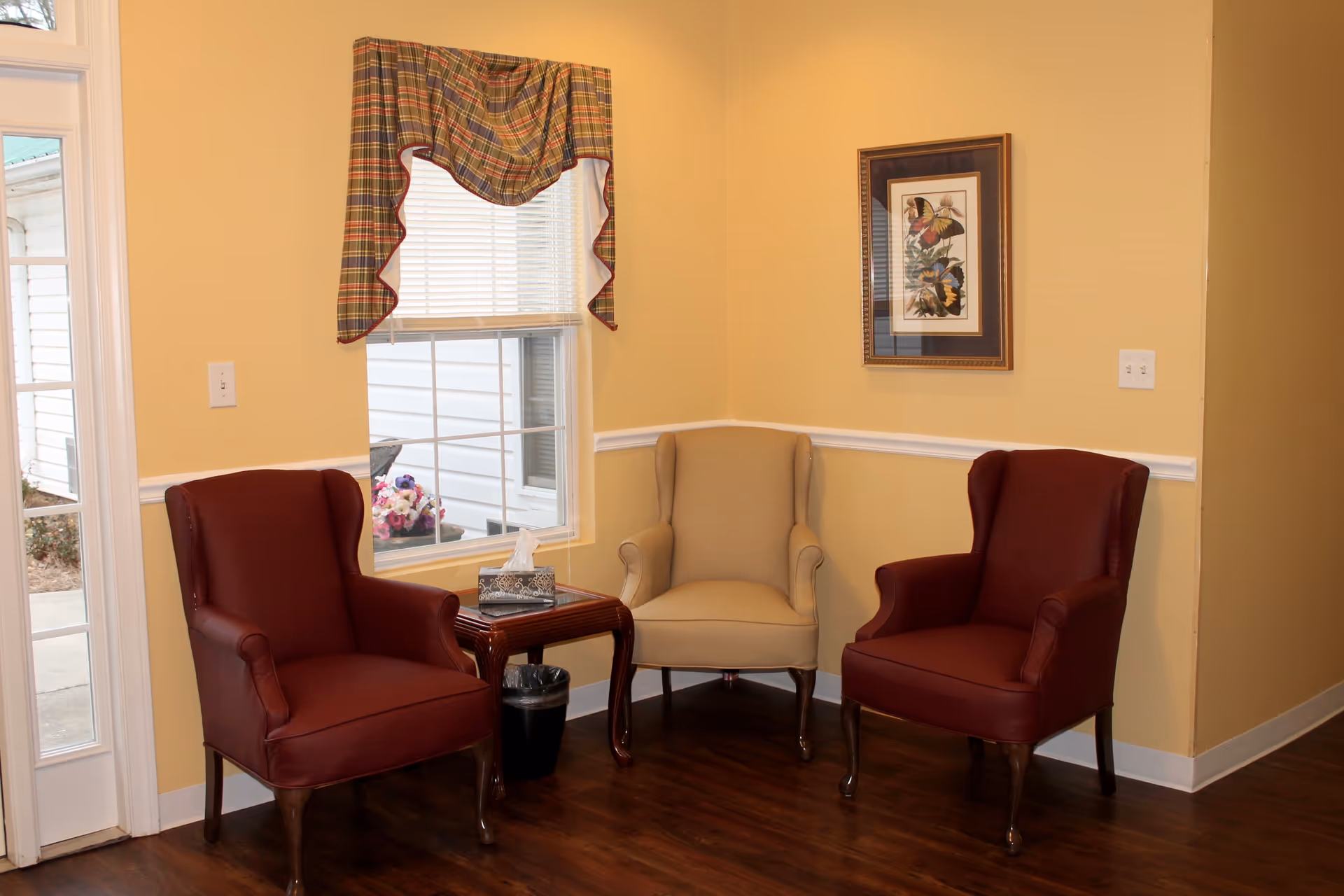 Three upholstered armchairs arranged around a small side table in a cozy seating area with a window and framed artwork.